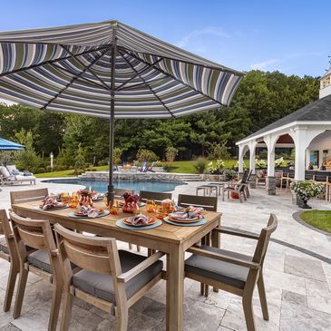Elegant backyard patio with dining table and pool in background.
