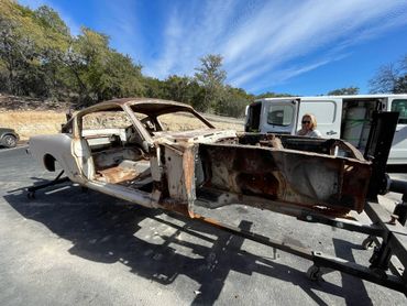 Rusty car frame being examined outdoors under a clear blue sky.
