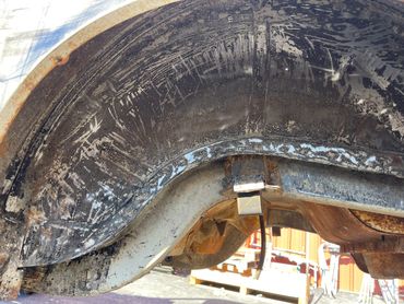Rusty and scratched metal vehicle wheel well showing wear and corrosion.