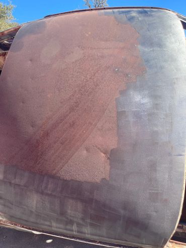 Rusty car roof partially covered with black tape under clear sky.