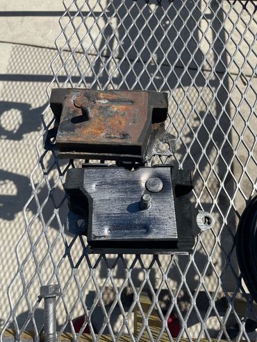 Comparison of old rusty and new shiny automotive engine mounts on a metal mesh table.