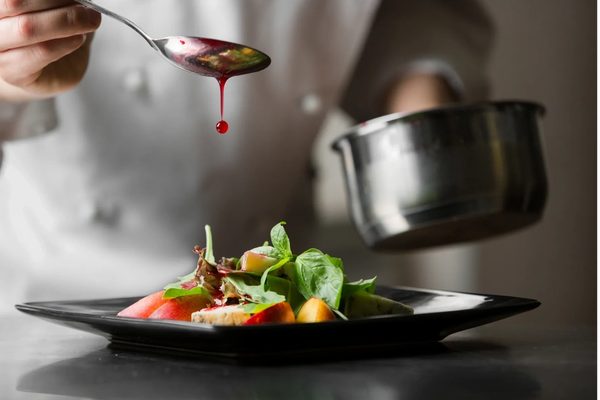 Chef drizzling red sauce on fresh salad.