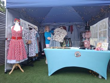 Vintage clothing stall with dresses and accessories under a blue canopy.