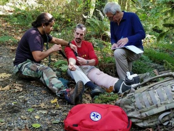 Two men assisting an injured man with a leg cast outdoors.