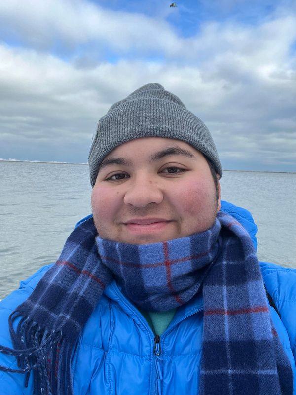 Person smiling by a body of water on a cloudy day.