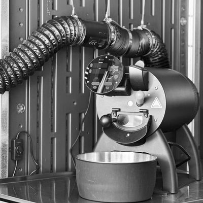 Industrial coffee roasting machine with ventilation system in a metal enclosure.