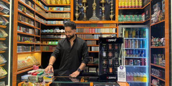 Man behind counter in a well-stocked tobacco shop with hookahs and Zippo lighters.