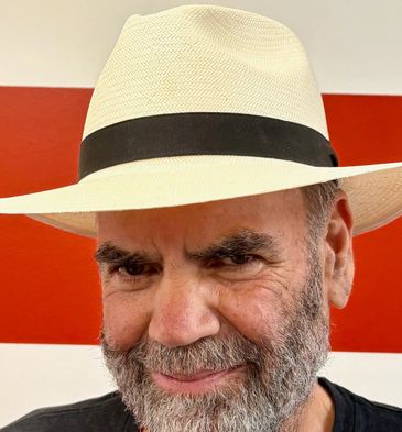 Man with gray beard wearing a white hat with a black band.