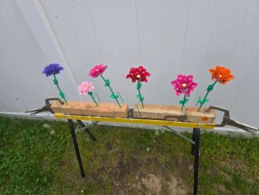 Colorful metal flowers clamped on wooden blocks outdoors.