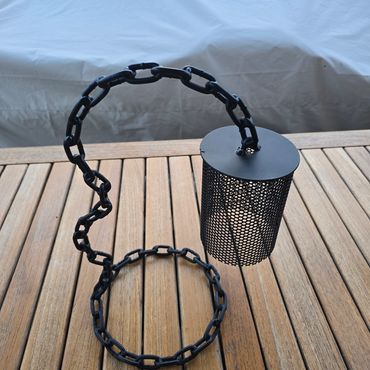 Black metal lantern with a chain on a wooden surface.