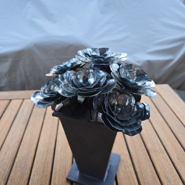 Metal flower sculpture in a black vase on a wooden table.