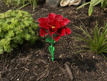 A red metal flower decoration planted in soil among green plants.
