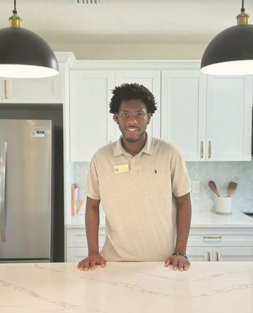 Man standing in a modern kitchen with white cabinetry and marble countertops.