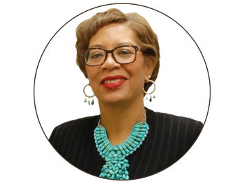 Smiling woman with glasses and turquoise necklace.