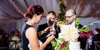 Three people dressed formally socializing at an event with a decorated cake.
