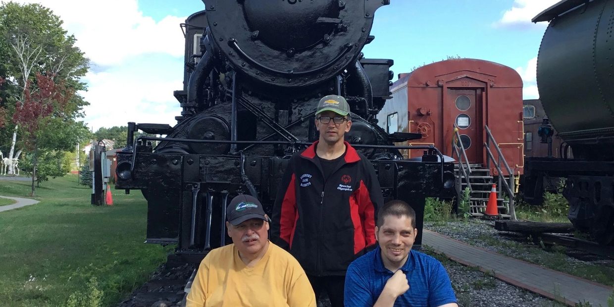 Trois clients des SHDS prennent la pose devant un vieux train.