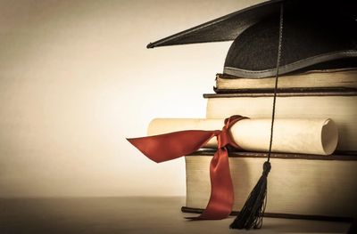 sepia image of 3 stacked books with a scroll and mortar board graduation hat