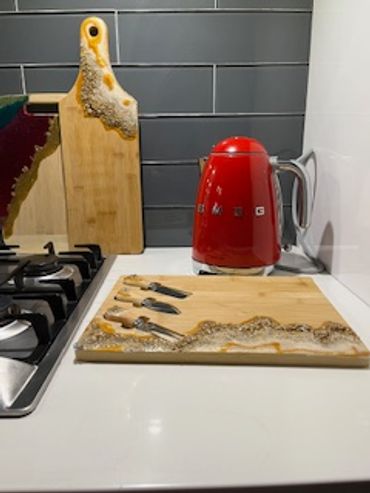 Resin-embellished wooden cutting boards and a red electric kettle on a kitchen counter.