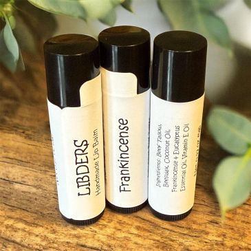 Three labeled lip balm tubes on a wooden surface with green leaves.