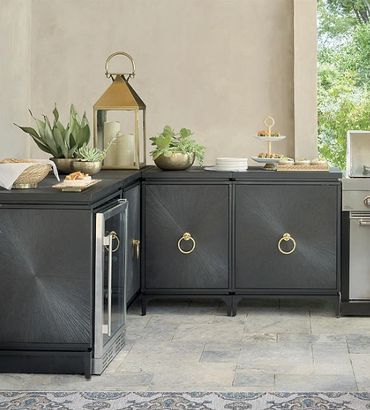 Modern outdoor kitchen setup with black cabinets, plants, and a lantern.