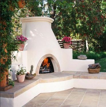 Outdoor white stucco fireplace with potted flowers and firewood in a garden.