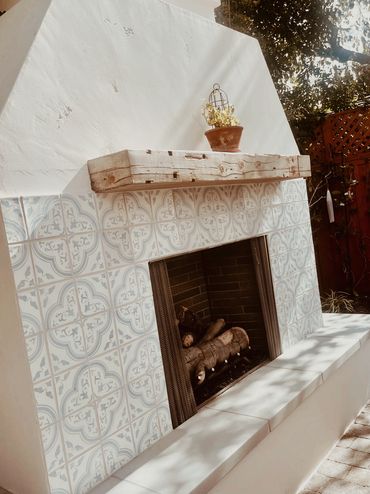 Outdoor fireplace with patterned tiles and rustic wooden mantel.