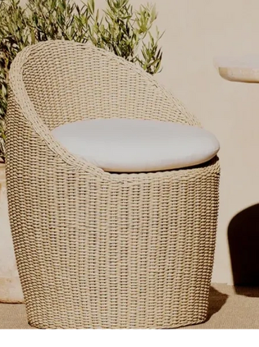 Wicker chair with cushion beside a wooden table and potted plant.