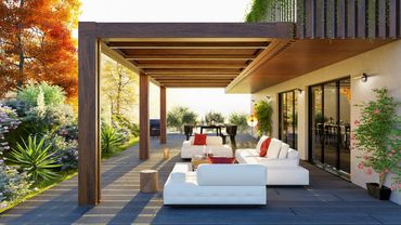 Modern outdoor patio with white sofas and wooden pergola surrounded by vibrant autumn foliage.