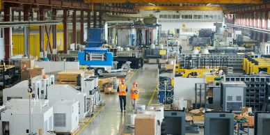 Two workers walk through a large industrial factory filled with machinery.