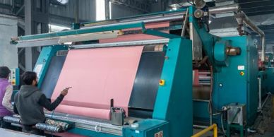 Workers inspecting fabric on a large industrial textile machine.