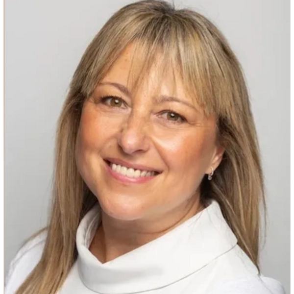 Smiling woman with blonde hair and white top against a plain background.