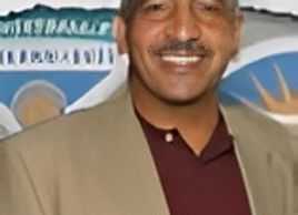 Smiling man wearing a blazer and maroon shirt.