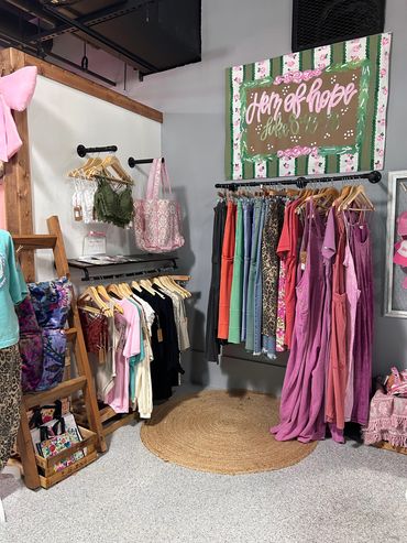 Boutique corner with colorful clothes, bags, and a decorative sign on the wall.