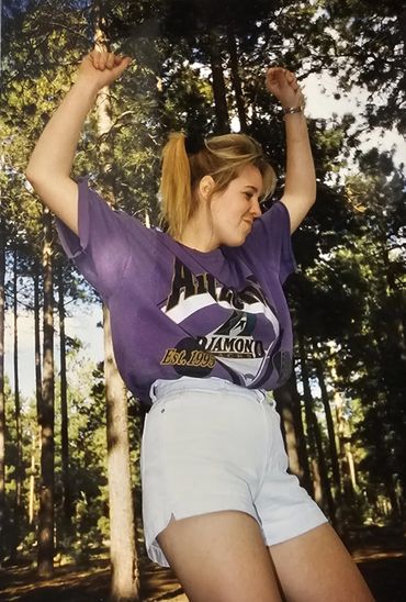 Young woman dancing joyfully outdoors in a forest setting.