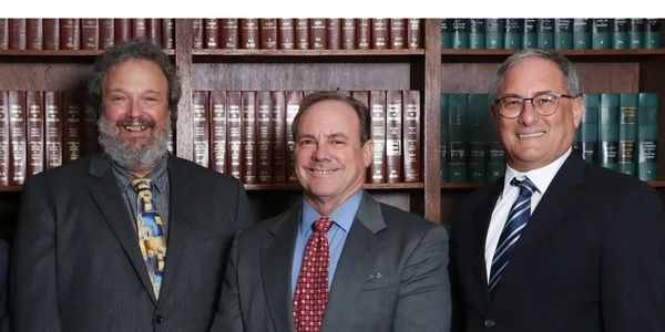 Three men in suits standing in front of shelves filled with books.