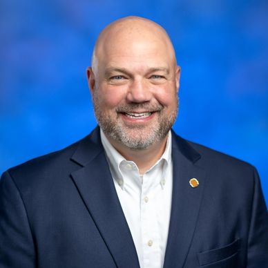 Smiling bald man in a suit with a blue background.
