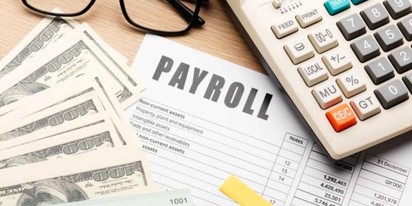 Payroll document with cash, glasses, and a calculator on a wooden desk.