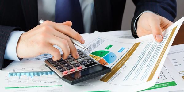 Person using a calculator and analyzing financial documents with charts and graphs.