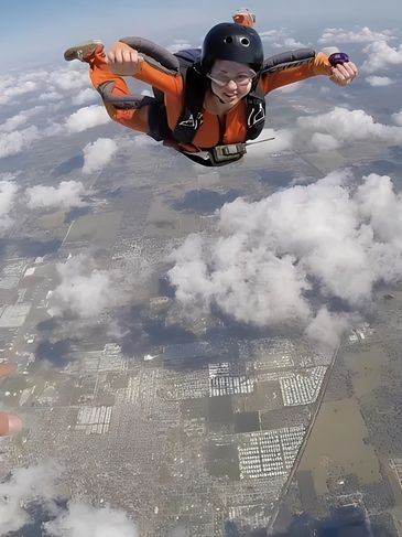 Solo skydiver under canopy landing in a field.