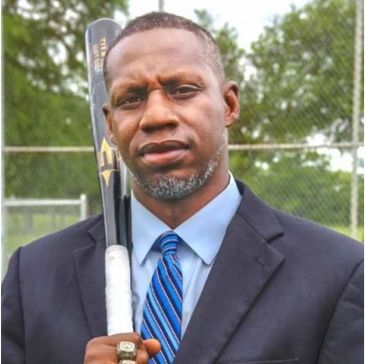 Man in suit holding a baseball bat with a serious expression outdoors.