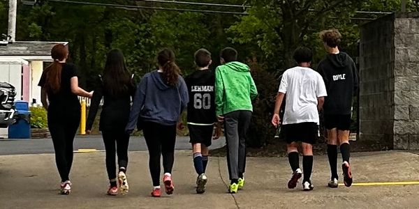 A group of seven teenagers walking away together on a paved path.