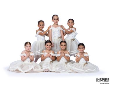Seven young ballerinas posing in white tutus.