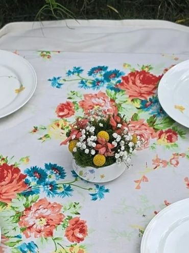 A floral centerpiece on a colorful flower-patterned tablecloth with white plates.