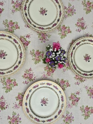 Vintage floral plates arranged around a small flower bouquet on a matching floral tablecloth.