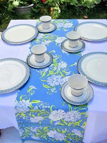 Elegant outdoor table setting with blue floral runner and matching china.