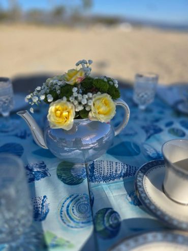 A teapot with yellow flowers on a blue seashell-patterned tablecloth.