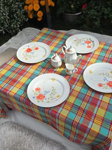 A colorful plaid tablecloth with floral porcelain tea set and plates outdoors.