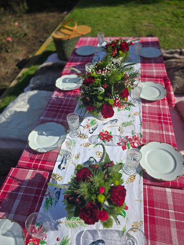 Outdoor table set with red plaid tablecloth and floral centerpieces.