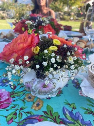 Colorful bouquet centerpiece on a floral tablecloth at an outdoor gathering.