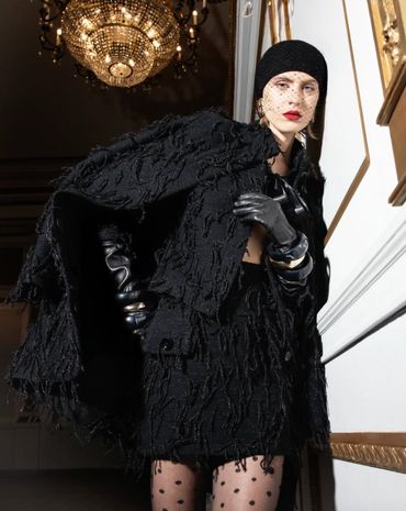 Fashion model in elegant black textured outfit with gloves and veil under chandelier.